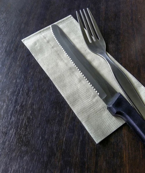 Knife and fork at napkin on wooden background — Stock Photo, Image