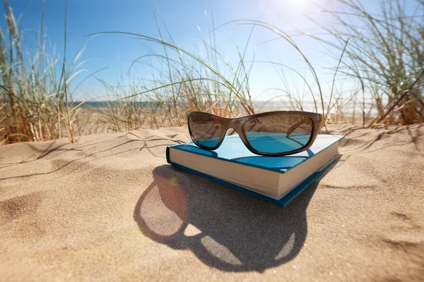 Buch und Sonnenbrille am Strand — Stockfoto