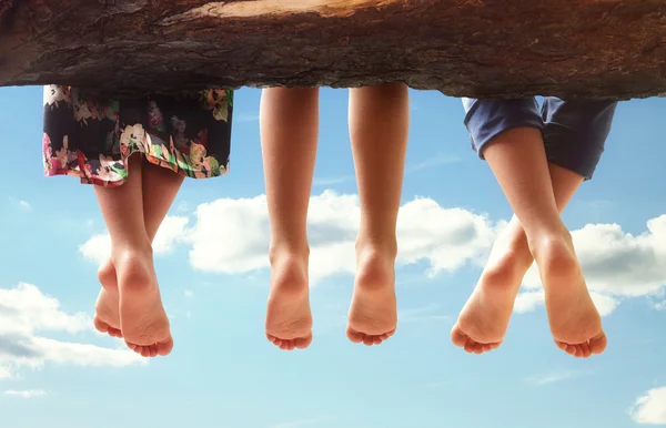 Des enfants assis dans un arbre suspendant leurs pieds — Photo