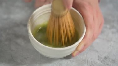 Beyaz bir kasede bambu şampanyası ile harmanlanmış yeşil çay tozu ve sıcak su taşıyan bir kızın ellerinde. Ev yapımı eşleşmesi