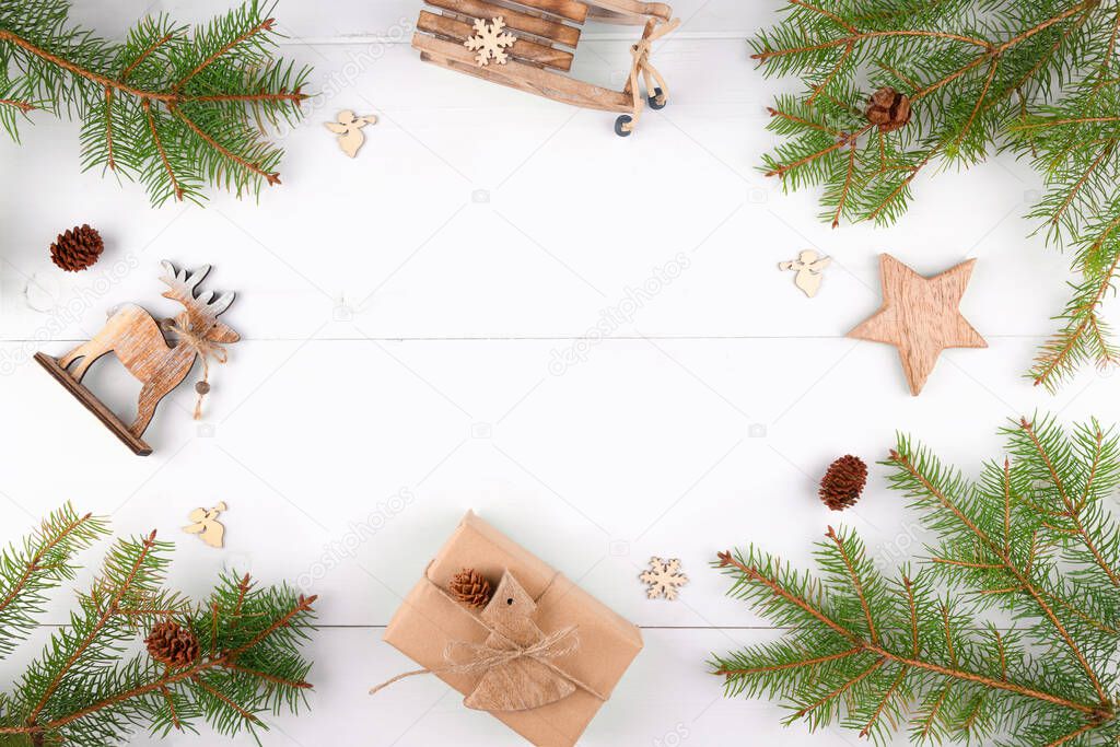 Christmas background frame of fir twigs, wooden zero waste home decoration: reindeer, stars and chistmas tree on white background, top view. Reusable sustainable recycled decor. Eco friendly new year