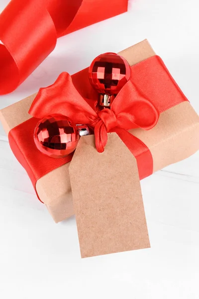 Tag de presente de Natal mock up com caixa de presente envolto em papel reciclado artesanal com laço de fita vermelha em um backgroud branco — Fotografia de Stock