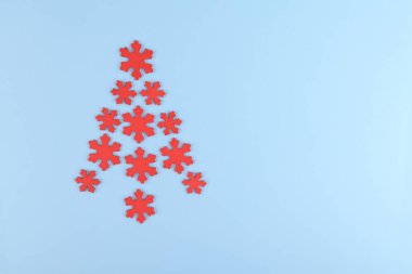 Alternative Christmas tree made from red wooden snowflakes decoration on a light blue background. Copy space, flat lay