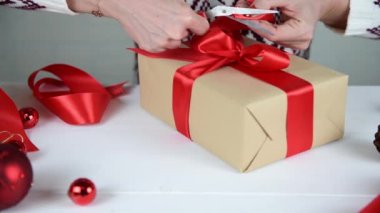 4K kadın eli Kraft kağıt hediye kutusunda kırmızı kurdele yapıyor. Noel ve Yeni Yıl için hediye hazırlıyorum.