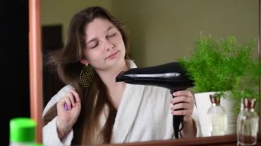 4k Beautiful young woman drying long hair with dryer, looking in the mirror. Morning routine concept