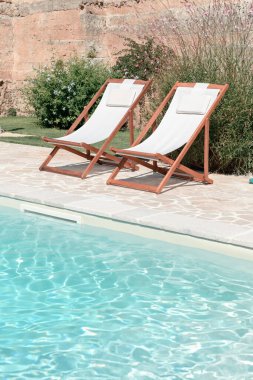 Açık mavi suyla yüzme havuzu ve güneşli bir bahçede güneşli bir günde iki güneş yatağı, rahatlama ve rahatlama için güzel bir tatil, farkındalık anlayışı, mutluluk ve yavaş yaşam.