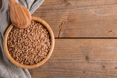 Tahta arka planda kepekli çiğ, hecelenmemiş farro.
