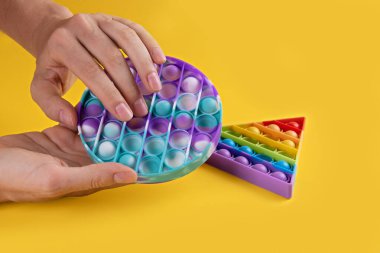 Sarı arka planda çocuklar ve yetişkinler için pastel renkli, yuvarlak popit oyuncak antistresi kullanan kadın hanlar. Esnek duyusal stres önleyici oyuncak, onu yuvarlak hale getir, boşluğu kopyala