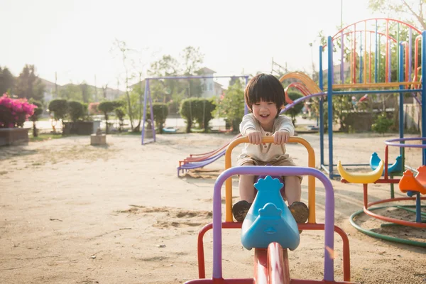 Criança montando bordo de balancé no parque infantil sob a luz do sol — Fotografia de Stock