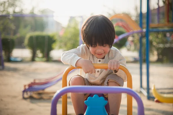 Criança montando bordo de balancé no parque infantil sob a luz do sol — Fotografia de Stock