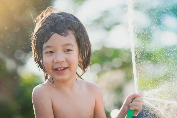 Carino asiatico ragazzo ha divertente giocare in acqua da un tubo all'aperto — Foto Stock