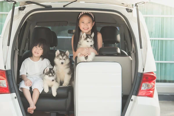 Happy asian children and siberian husky puppy sitting in the car