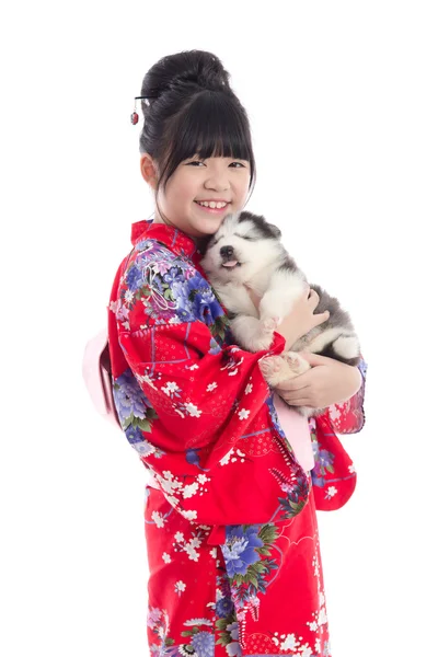 Liten asiatisk flicka i röd kimono leker med en siberian husky pu — Stockfoto