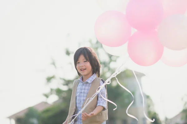 Süße asiatische Kind mit vielen Luftballons spielen im Park unter su — Stockfoto