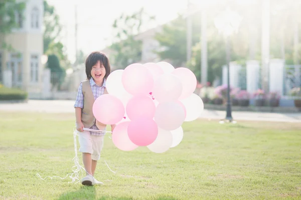 Bonito criança asiática com muitos balões brincando no parque sob su — Fotografia de Stock