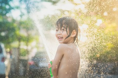 Yakışıklı Asyalı çocuk dışarıda hortumla oynarken eğleniyor.
