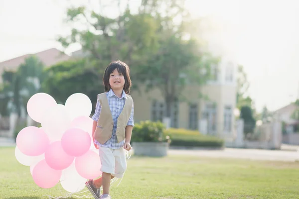 Дитина з багатьма повітряними кулями біжить в парку під сонячним світлом — стокове фото