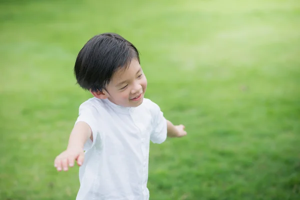 Asiatiska barn i vita cothes spelar på grönt gräs — Stockfoto