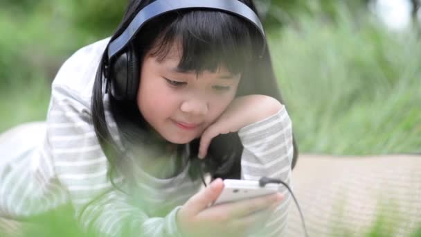 Hermosa chica asiática escuchando música en el parque — Vídeo de stock
