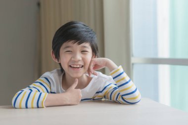 Asyalı şirin bir çocuk ahşap masada çenelerini dinlendiriyor.