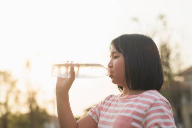 Güzel Asyalı kız açık havada bir şişeden su içiyor.