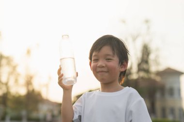 Yakışıklı Asyalı çocuk açık hava şişesinden su içiyor.