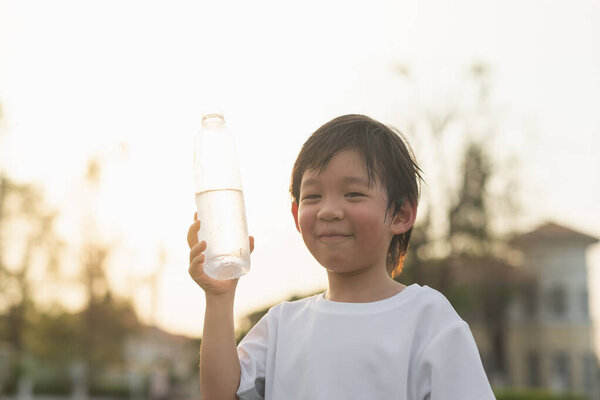 Милый азиатский мальчик пьет воду из бутылки на открытом воздухе