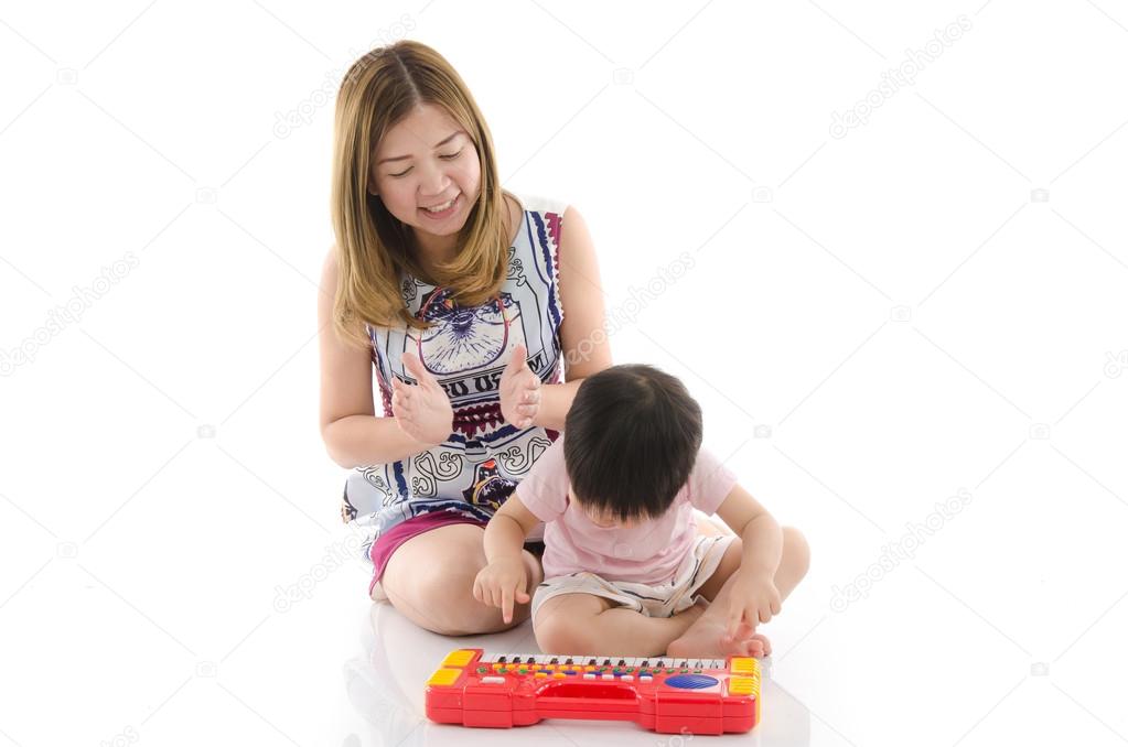 Cute mother teach her son kid to play electrical toy piano 