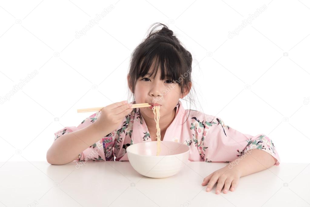 Little asian girl wearing kimono and eating noodles 