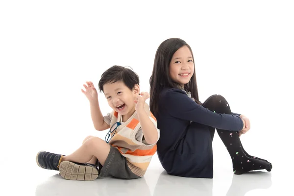 Zwei glückliche asiatische Kinder sitzen und lehnen sich aneinander — Stockfoto