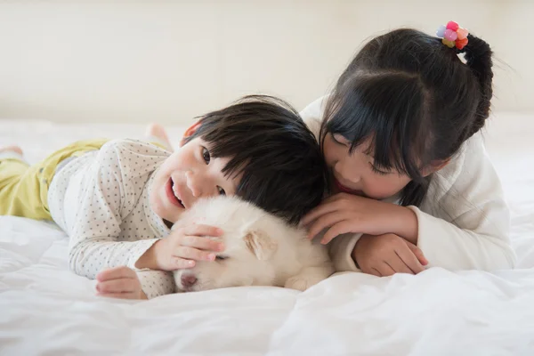 Enfants et chiot s'amuser couché au lit — Photo