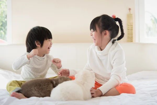 asian children kissing puppy on white bed
