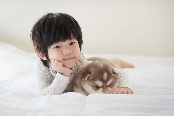 白いベッドの上に横たわる子とシベリアン ハスキーの子犬 — ストック写真