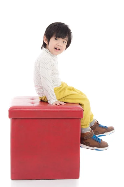 Ładny azjatycki chłopiec siedzi na stołku czerwony na białym tle — Zdjęcie stockowe