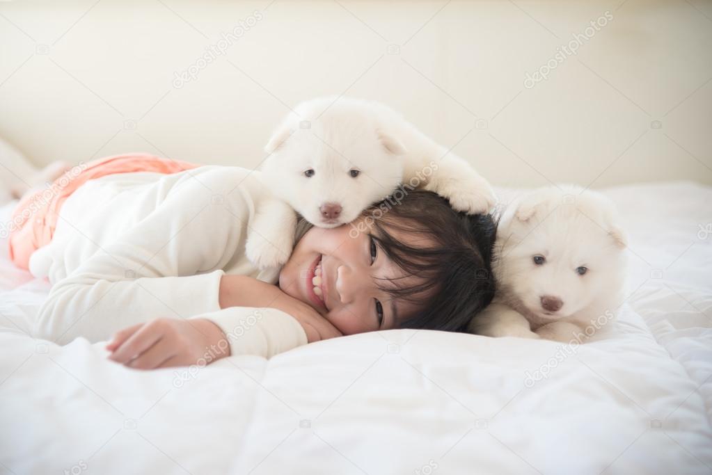 asian girl lying with two siberian husky puppies on bed