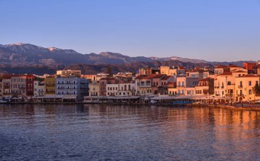 Sunrise at Old Venetian harbour of Chania, Crete, Greece, shop, hotels, cafes and restaurants on its quay in first sunrays. Cretan hills and mountains