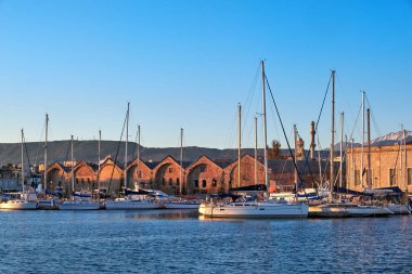 Sunrise in Old Venetian port, Chania, Crete, Greece. Sailing boats, yachts, pier, Old Venetian shipyard. Bell tower of Greek church, Cretan mountains