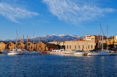 Old Venetian port, Chania, Crete, Greece. Sailboats, yachts, pier, shipyards or Arsenali Veneziani or Neoria. Bell tower and minaret, Cretan mountains