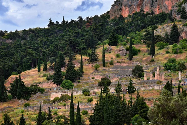 Pohled na slavný antický řecký komplex - Delphi oracle. Zřícenina chrámu Apollónova a divadla. Turisté spěchají sem a tam po stezkách mezi borovicemi a cedry — Stock fotografie