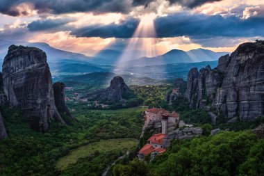 Moni Agias Varvaras Roussanou 'nun manastırı ve Meteora, Yunanistan ve Vadi' nin kayaları. Bulutlu gökyüzü, güneş ışınları düşüyor. UNESCO Dünya Mirası