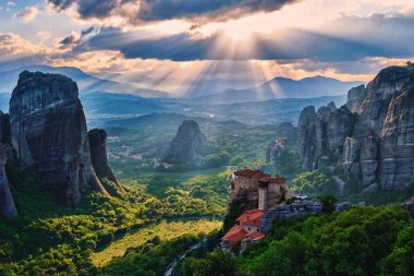 Moni Agias Varvaras Roussanou 'nun manastırı ve Meteora, Yunanistan ve Vadi' nin kayaları. Bulutlu gökyüzü, güneş ışınları düşüyor. UNESCO Dünya Mirası