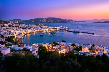 Mykonos, Cyclades, Yunanistan, liman ve liman, gemi, badanalı evler üzerinde gün batımından sonra renkli bir manzara. Renkli kasaba aydınlanıyor.