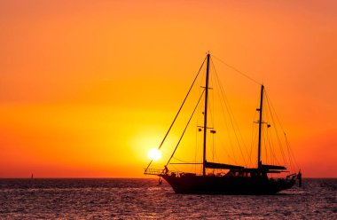 Güneşin batışında yelkenli teknenin silueti, deniz sularında güneş parlıyor. Romantik deniz manzarası, güneş baş yelkenlere dokunuyor..