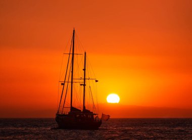 Güneşin batışında yelkenli teknenin silueti, deniz sularında güneş parlıyor. Romantik deniz manzarası. Yelkenli, denize git.
