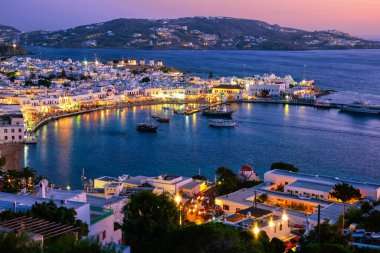 Mikonos, Yunanistan, liman, gemiler, beyazlatılmış evler gün batımından sonra renkli bir manzara. Kasaba ışıkları yanıyor. Tatiller, eğlence, Akdeniz yaşam tarzı