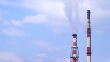 Mavi gökyüzü ve bulutlardaki birleşik ısı ve güç istasyonunun 4k zaman kaydında iki baca. Rüzgarda sallanan beyaz duman.