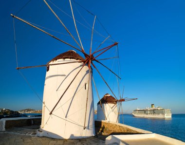 Yunanistan 'ın ünlü Mykonos turistik merkezi. Geleneksel bembeyaz yel değirmenleri denizden ve yolcu gemisiyle limandan ayrılıyor. Günaydın, yaz, açık mavi gökyüzü