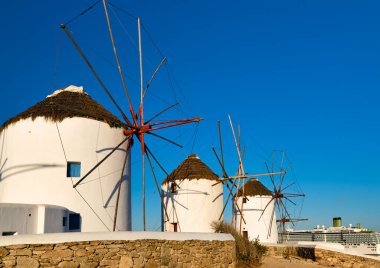 Yunanistan 'ın ünlü Mykonos turistik merkezi. Geleneksel bembeyaz yel değirmenleri, yaz, mavi gökyüzü, yolcu gemisi. Seyahat hedefi, ikonik görünüm.