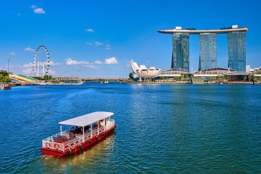 Marina Bay Sands, Shoppes AVM, ArtScience Müzesi ve Singapur 'daki Helix Köprüsü' ne yaklaşan turist teknesi. Singapur Flyer gözlem çemberi uzakta. Güneşli gün, açık mavi gökyüzü
