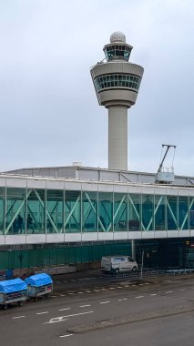 Amsterdam, Hollanda - 12 Aralık 2023 Schiphol havaalanı AMS 'nin ikonik hava trafik kontrol kulesi ve yolcu köprüsü. Avrupa 'nın büyük havacılık merkezi, uluslararası seyahatin sembolü. Hava bulutlu, yer araçları, bagaj arabaları, ulaşım